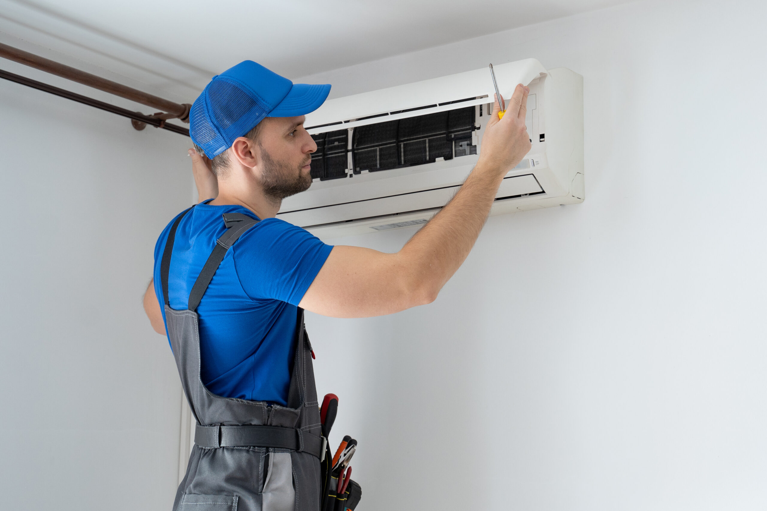 male technician overalls blue cap repairs air conditioner wall scaled